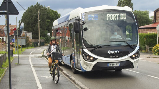Photo d'une cycliste sur un VAE à côté d'un bus évéole